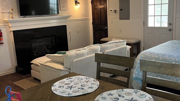 A living room with a fireplace, a television, a dining table with placemats, a ceiling fan, and a skylight. - Highlands cottage across the street from Proving Ground and Twin Lights Marina (Highlands)