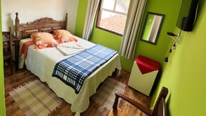 A bedroom with a wooden bed, a bedside table, a chair, a window with curtains, a mirror, and a green wall. - Pousada Cantinho Gostoso (Ouro Preto)