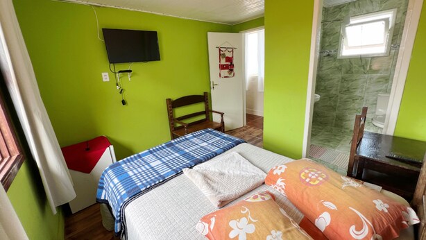 A room with a bed, a chair, a television, and a door leading to a bathroom. - Pousada Cantinho Gostoso (Ouro Preto)
