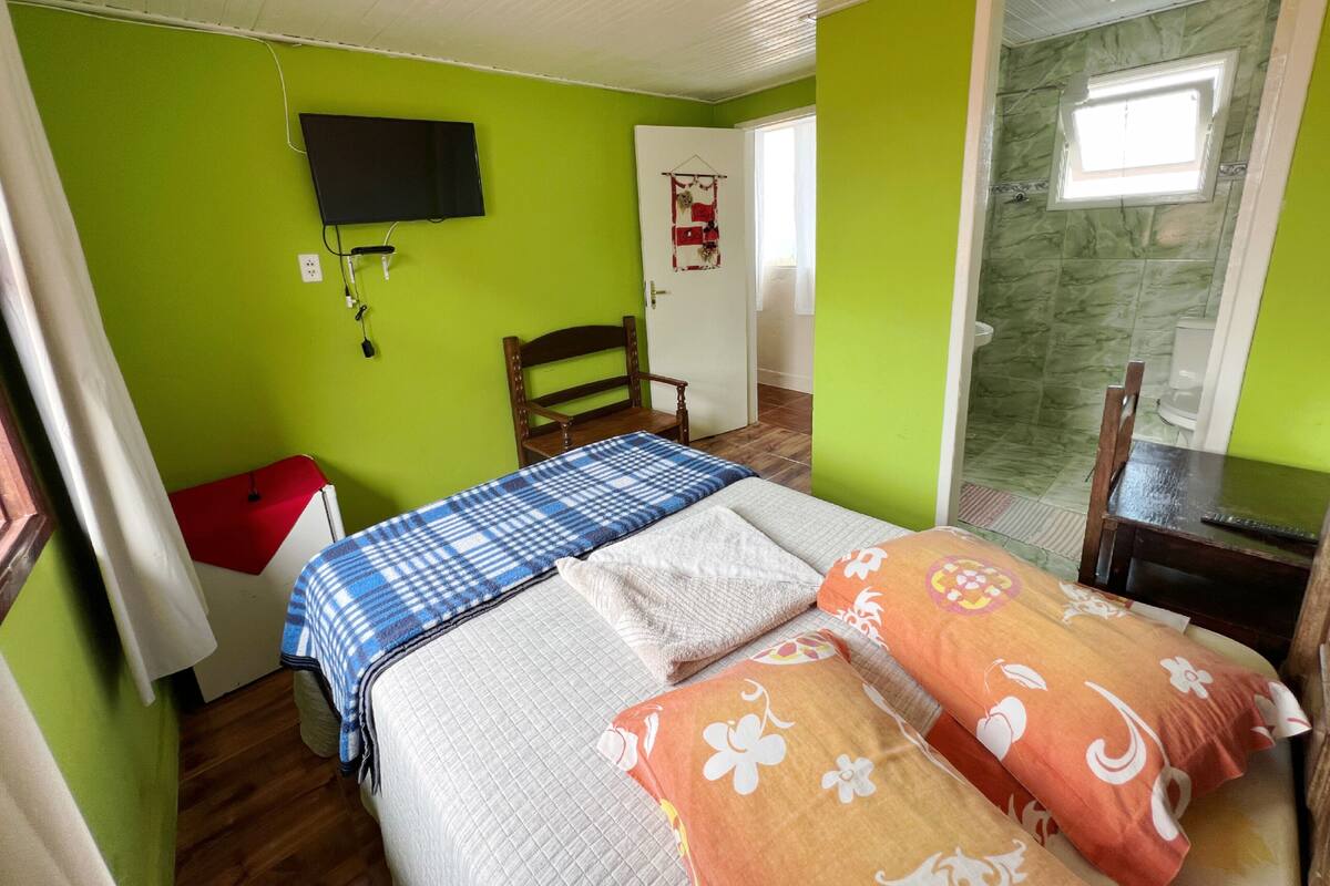 A room with a bed, a chair, a television, and a door leading to a bathroom.