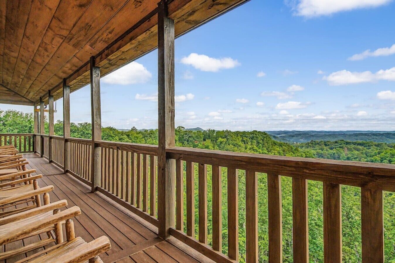 Een houten terras met een hekwerk, banken en uitzicht op een bebost landschap.