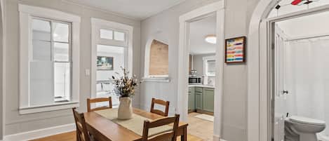 A dining area with a wooden table and chairs, a vase with flowers, and a hanging light fixture.