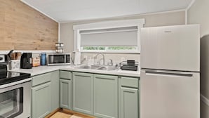 A modern kitchen with a built-in microwave, a sink, a white refrigerator, and a window with a view of greenery.
