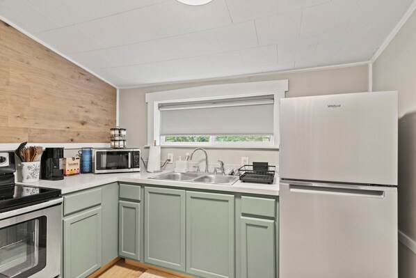 A modern kitchen with a built-in microwave, a sink, a white refrigerator, and a window with a view of greenery.