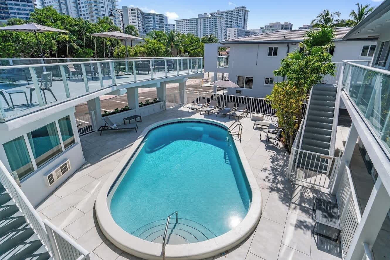 A rooftop swimming pool with a glass balustrade, lounge chairs, and a staircase leading to an upper level.