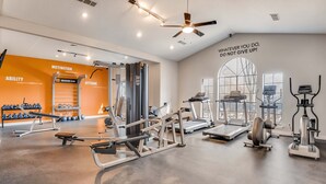 A gym with various exercise equipment, motivational wall text, and a large window providing natural light.