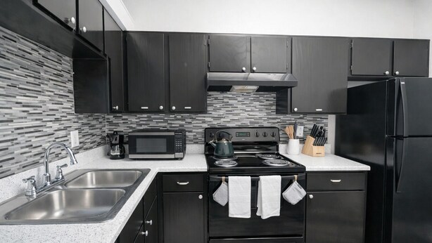 A modern kitchen with dark cabinets, a stainless steel sink, a microwave, a stove, and a refrigerator.