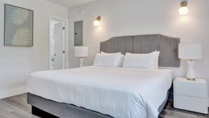 Une chambre à coucher moderne avec un grand lit, des lampes de chevet, une table de nuit et une œuvre d’art encadrée au mur.