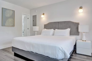 Ein modernes Schlafzimmer mit einem großen Bett, Nachttischlampen, einem Beistelltisch und einem gerahmten Kunstwerk an der Wand.