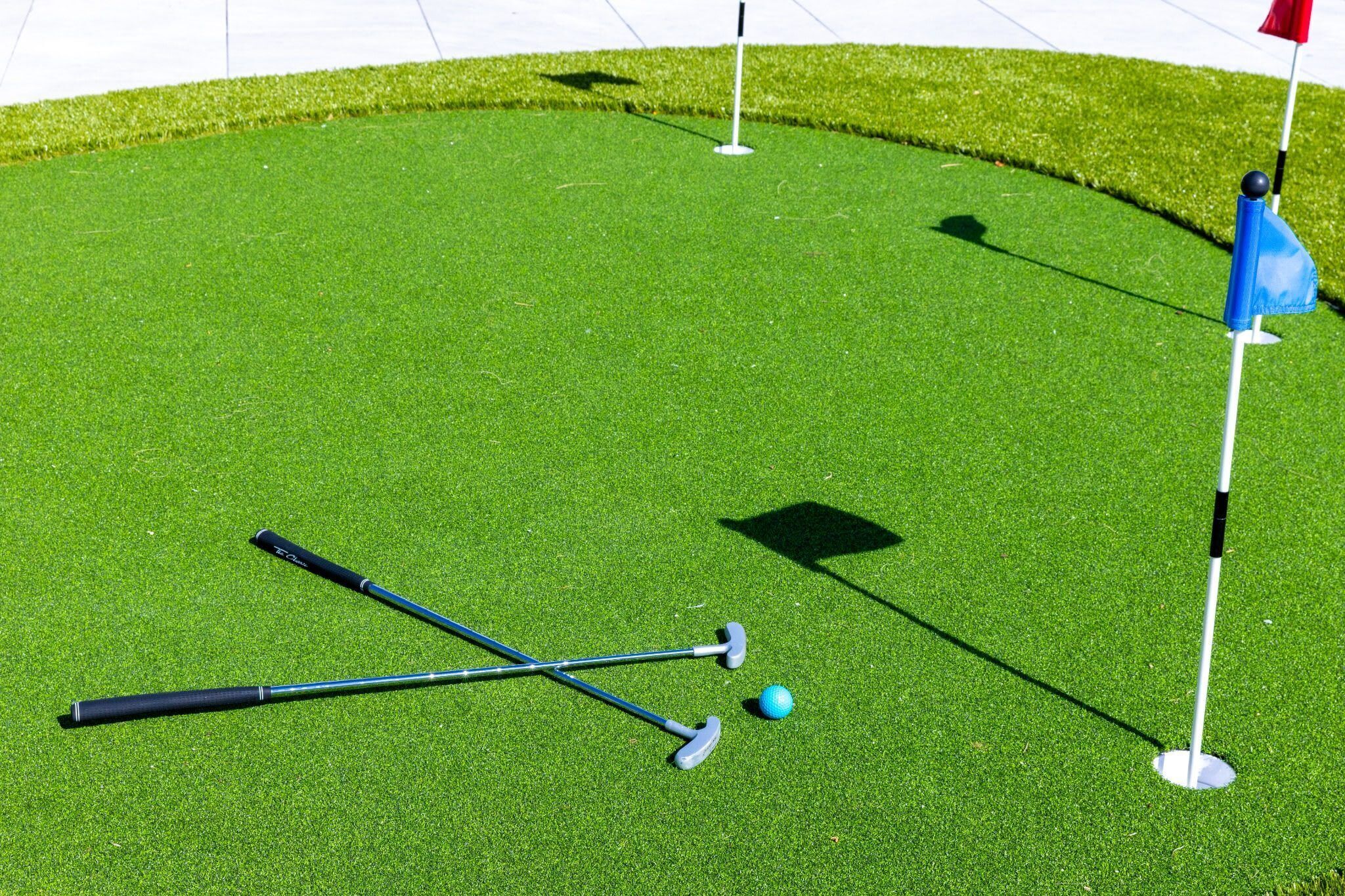 Een golfbaan met een putting green, een vlag en golfclubs.