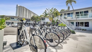 Une rangée de vélos d’appartement portant la marque « The Garden », un bâtiment moderne avec un escalier et un palmier en arrière-plan.