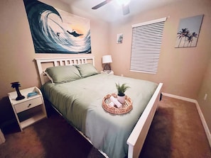 Ein Schlafzimmer mit Bett, Nachttisch, Lampe und Kunstwerk.