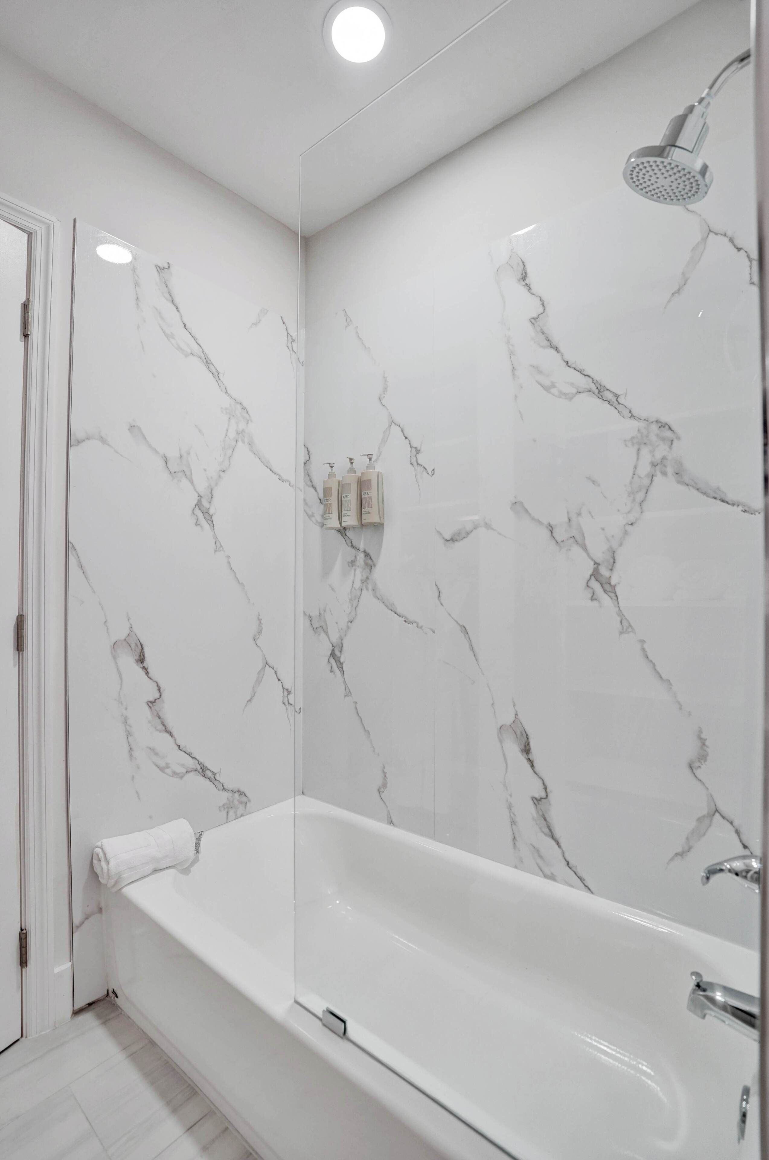 A modern bathroom with a marble wall, a bathtub, and a shower.