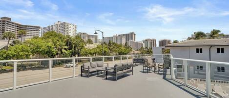 A rooftop terrace with outdoor seating, a view of the cityscape, and a clear sky.