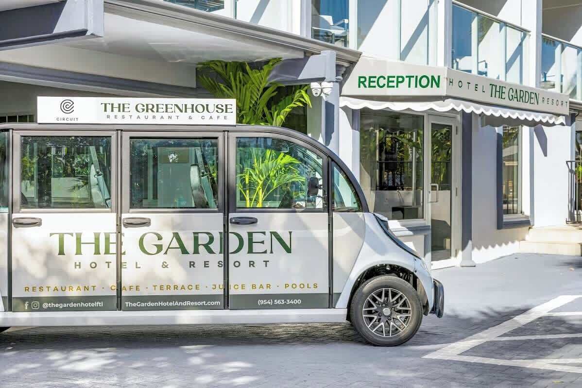 Ein weißer Van mit dem Schriftzug 'The Garden Hotel & Resort', geparkt vor einem Gebäude mit einem Empfangsbereich.