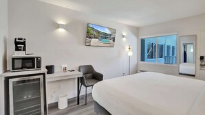 Habitación de hotel moderna con cama, escritorio, microondas y televisión mostrando vista a la piscina.