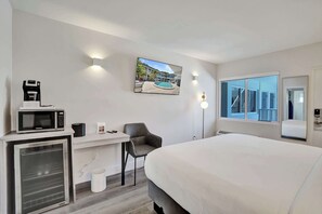 Ein modernes Hotelzimmer mit Bett, Schreibtisch, Mikrowelle und einem Fernseher, der Blick auf einen Pool bietet.