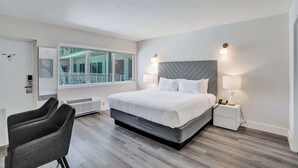 Una habitación de hotel moderna con una cama grande, lámparas de noche, una silla y una ventana con vistas a un balcón.