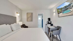 A hotel room with a large bed, a desk with a chair, a painting, and a view of a swimming pool. - Fort Lauderdale King Room at Botanica (Fort Lauderdale)