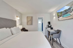 A hotel room with a large bed, a desk with a chair, a painting, and a view of a swimming pool. - Fort Lauderdale King Room at Botanica (Fort Lauderdale)