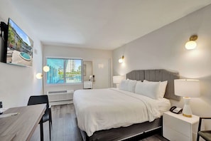 Ein Hotelzimmer mit Bett, Nachttischlampen, einem Schreibtisch und Blick auf einen Pool und Gebäude.