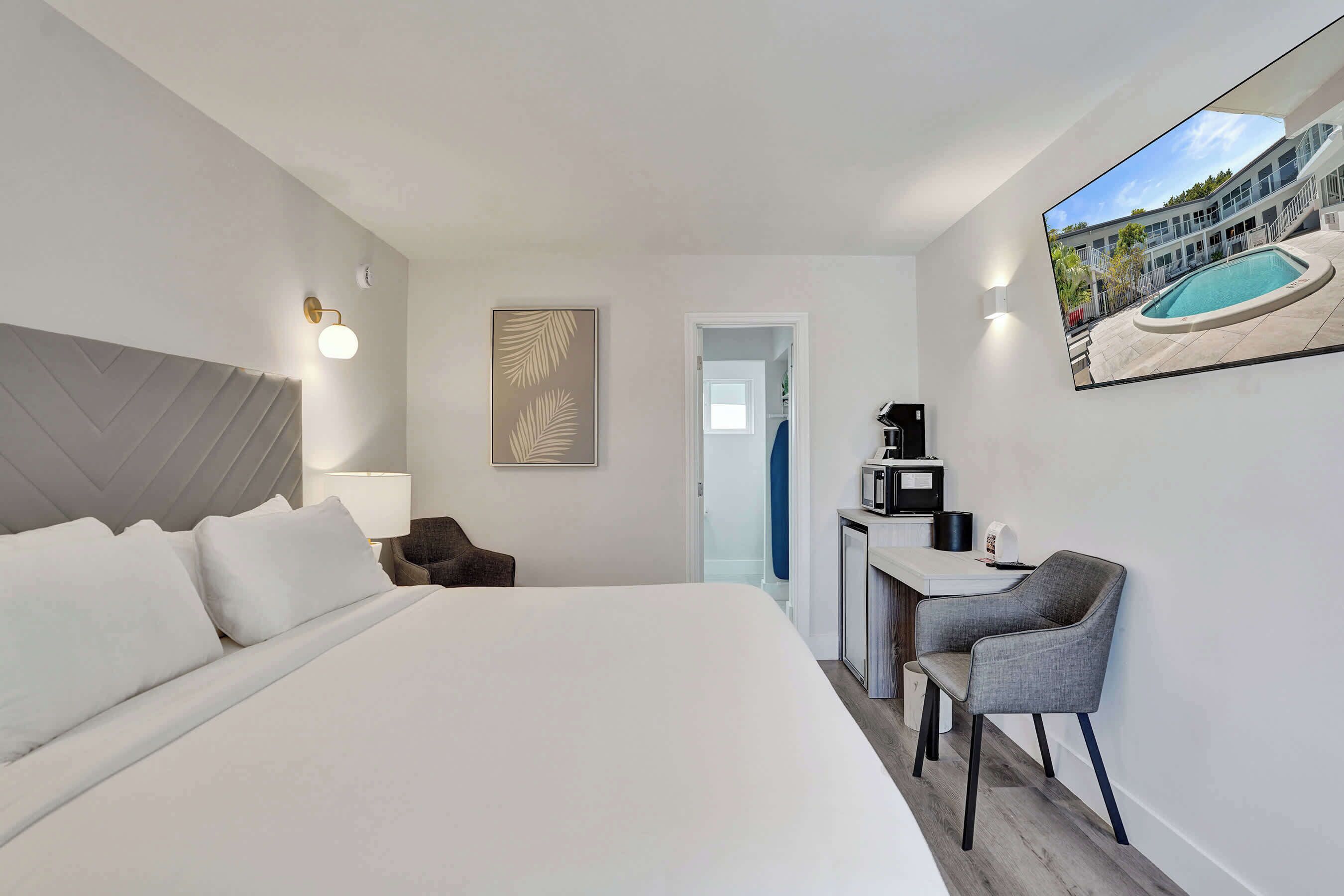 A hotel room with a large bed, a desk with a chair, a painting, and a view of a swimming pool.
