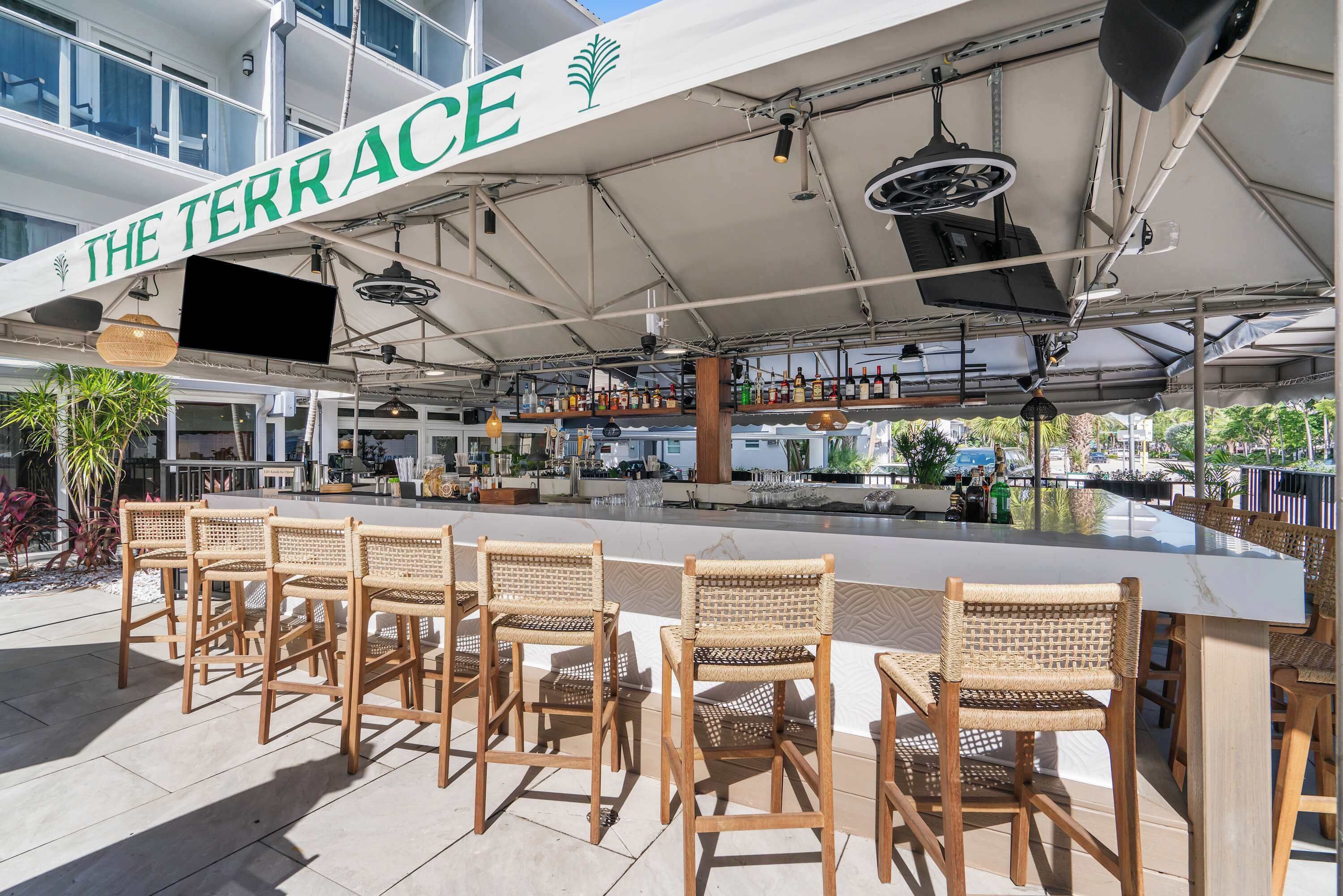 An outdoor terrace with a bar area, wicker chairs, and a sign reading 'THE TERRACE'.