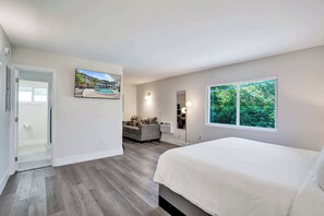 Ein Schlafzimmer mit einem Bett, einem Sofa, einem großen Fenster und einer Tür zu einem Badezimmer.