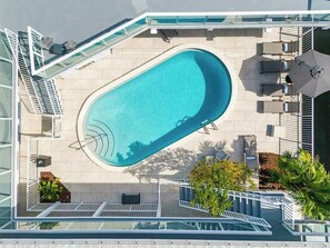 Ein Pool auf dem Dach mit Glasgeländer, Sitzgelegenheiten im Freien und einer Palme.
