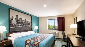 Ein Hotelzimmer mit Bett, Schreibtisch mit Fernseher, Stuhl, Fenster mit Vorhängen und einem Stadtbild an der Wand.