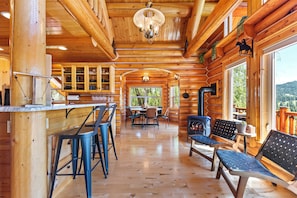A log cabin interior with a bar area, dining table, and seating.