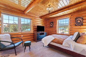 Ein Blockhauszimmer mit Bett, Sessel, Fernseher und großen Fenstern.