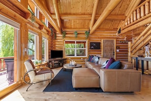 A log cabin interior with a sofa, armchair, and a television.