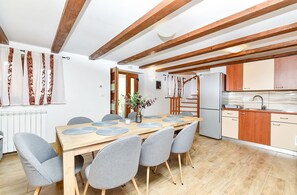 A modern kitchen with wooden beams, a dining area with a wooden table and grey chairs, and a refrigerator. - House 2442/251993 (Istria - Vodnjan), 8000m from the beach (Vodnjan)