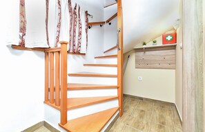Eine Holztreppe mit Handlauf, ein an der Wand befestigtes Regal mit Erste-Hilfe-Kasten und ein Blumentopf.