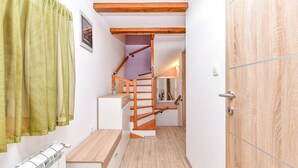 Un corridoio stretto con una scala in legno, un termosifone e una porta con stipite in legno.