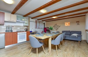 Een moderne keuken met houten balken, een eettafel met stoelen en een grijze bank.