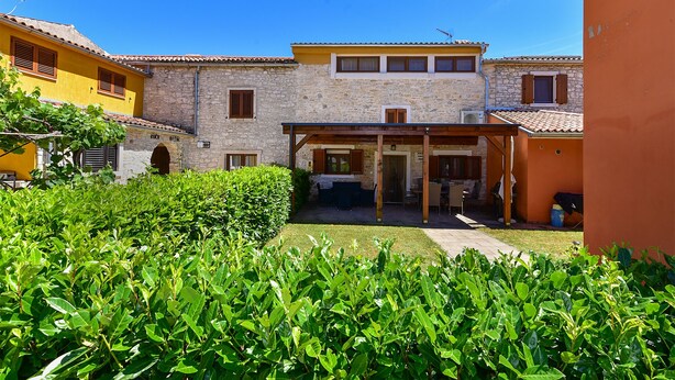 Un cortile con edifici in pietra, un'area salotto coperta e vegetazione lussureggiante.
