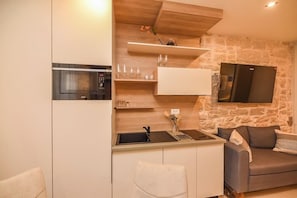 Eine kompakte Küche mit integriertem Mikrowellenherd, Spüle und flachbildschirmfernseher an einer Steinwand.