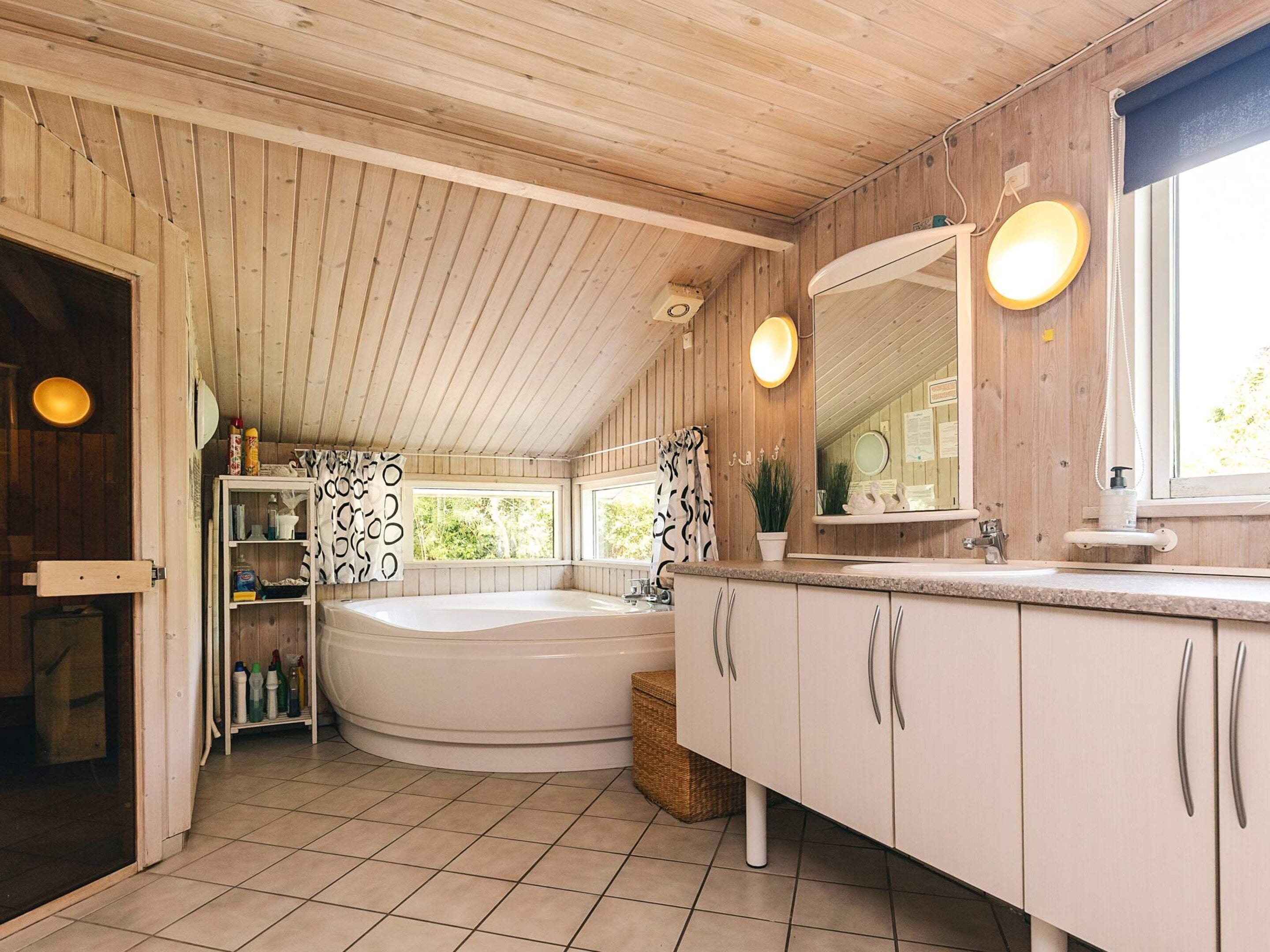 Een badkamer met een bad, een wastafel en een spiegel. Er zijn ramen en een deur.