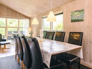 A dining area with a long table, multiple chairs, pendant lights, and a painting on the wall. - 10 Person Holiday Home in Rudkobing (Rudkobing)