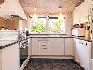 A modern kitchen with a black countertop, white cabinets, a double sink, and a window with a view of greenery. - 10 Person Holiday Home in Rudkobing (Rudkobing)
