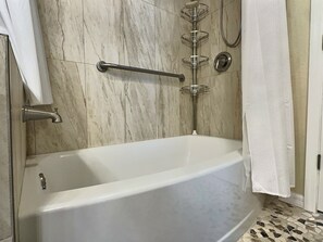 Ein Badezimmer mit einer Badewanne, einer Dusche, einem Handtuchhalter und einer Haltestange.