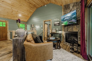 Un salon chaleureux avec une cheminée en pierre, un téléviseur fixé au mur et un plafond en bois.