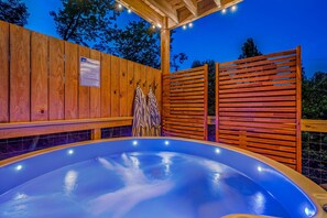 Ein Whirlpool mit Holzwänden und Fliesenboden, umgeben von einem Holzzaun und einem überdachten Bereich mit Beleuchtung.