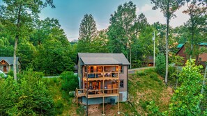 Eine mehrstöckige Holzhütte mit einem Balkon, umgeben von dichtem Wald.