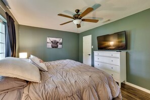 Une chambre à coucher avec un lit, un ventilateur de plafond, une télévision, une commode et une porte.