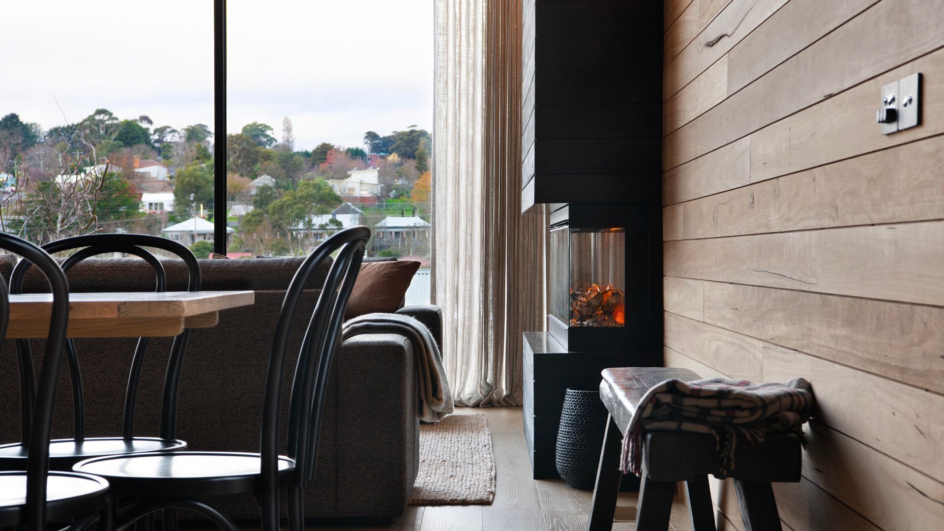 A cozy seating area with a fireplace, a view of the city, and a wooden wall.