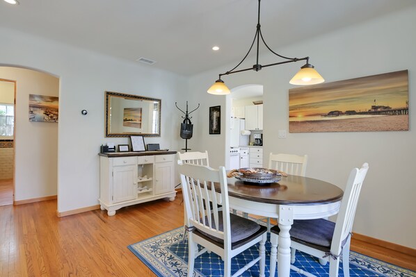 A dining area with a round table, white chairs, a blue patterned rug, and a painting of a sunset on the wall. - New! Casa Capricho in West Beach with A/C, private yard, walk to beach (Santa Barbara)