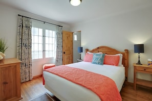 A bedroom with a bed, wooden headboard, bedside tables, a nightstand, a lamp, a potted plant, and a window with curtains. - New! Casa Capricho in West Beach with A/C, private yard, walk to beach (Santa Barbara)